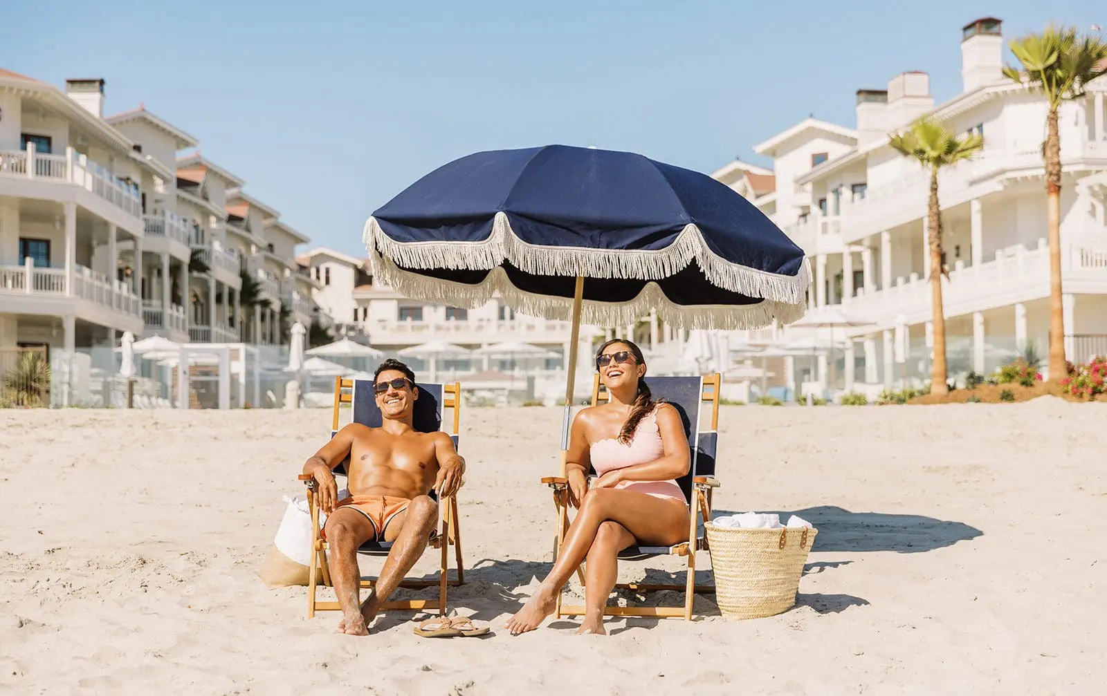 Couple sitting on the beach under an umbrella in front of Shore House at the Del