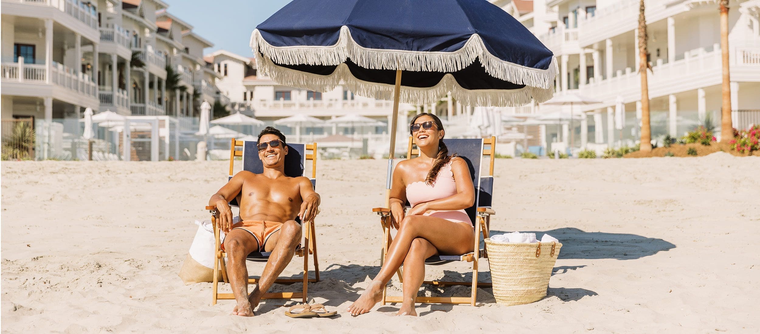 Couple sitting on the beach under an umbrella in front of Shore House at The Del